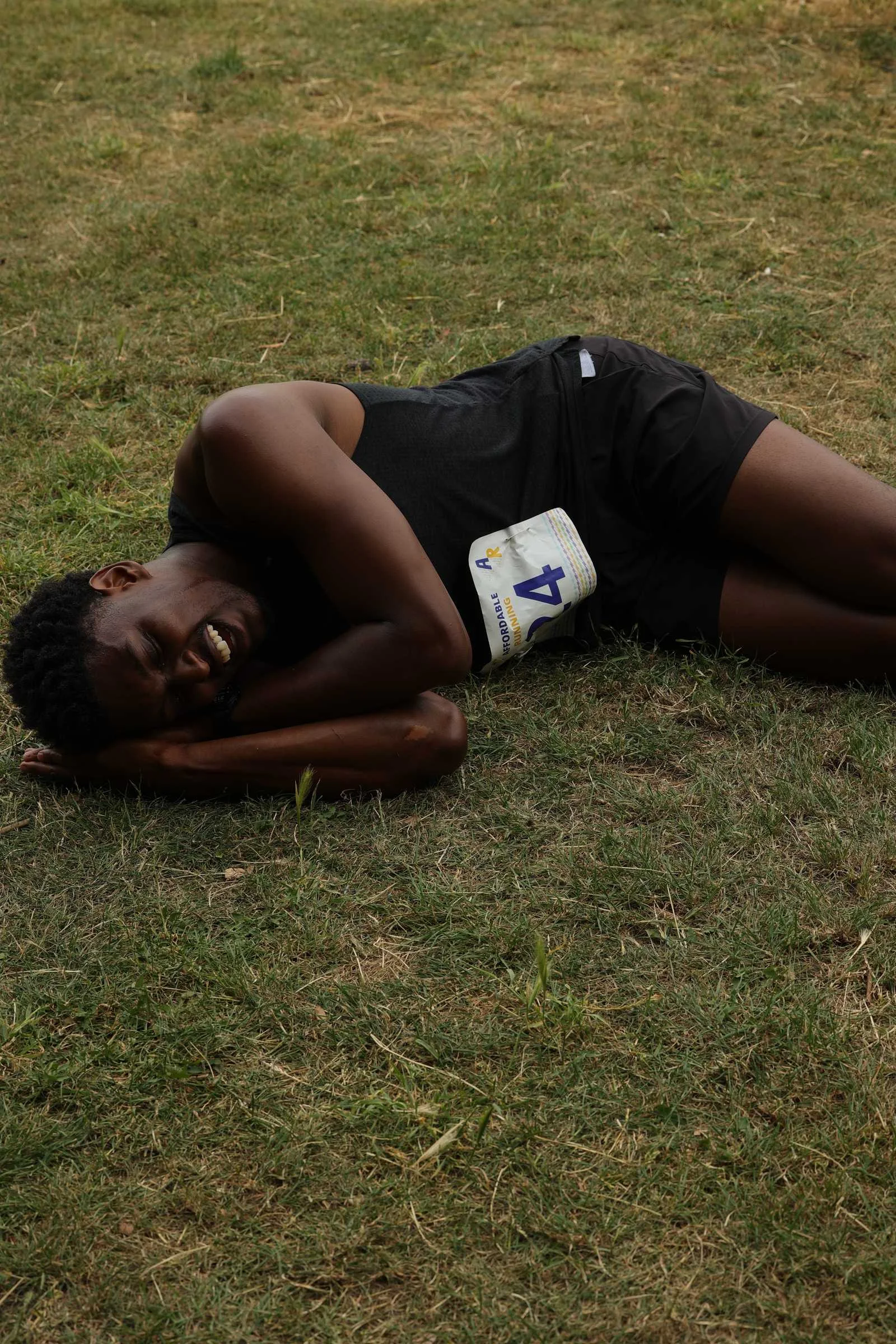 A runner smiling while resting on the grass after finishing